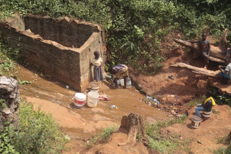 Village residents collect water polluted by the quarry at a water collection point they have developed at the foot of the mountain. Image © Yannick Kenné.