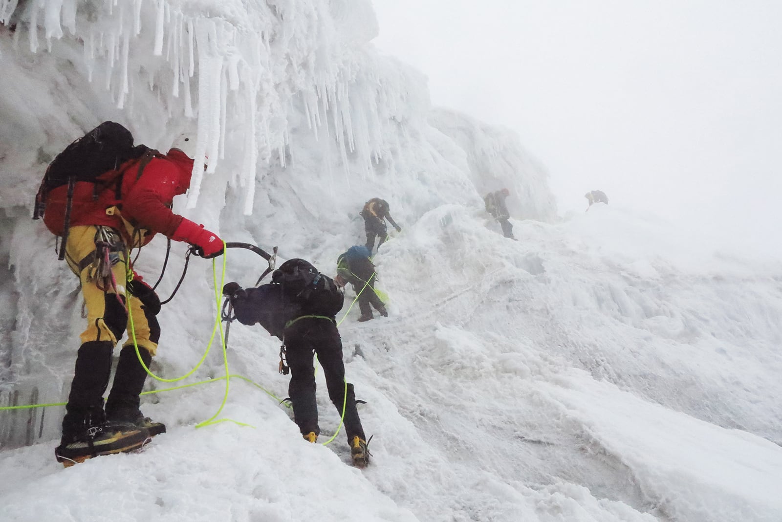 The trekking team connected by ropes traverse a snowy mountain landscape.