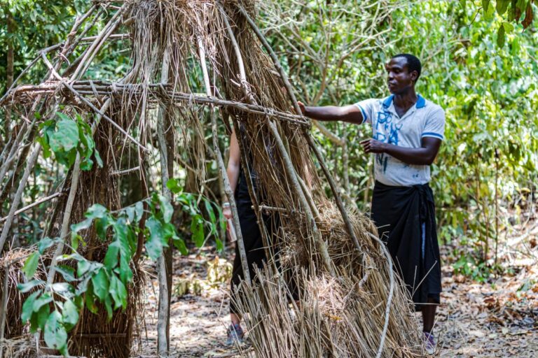 A tour guide gestures towards remnants of a shelter woven out of vines  in Kaya Kinondo, Coast region, Kenya. Image by Ninara via Flickr (CC BY 2.0)