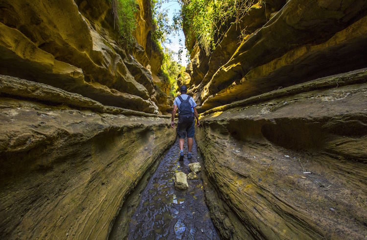 A woman hikes next to a waterfall in Hell's Gate National Park, Kenya.