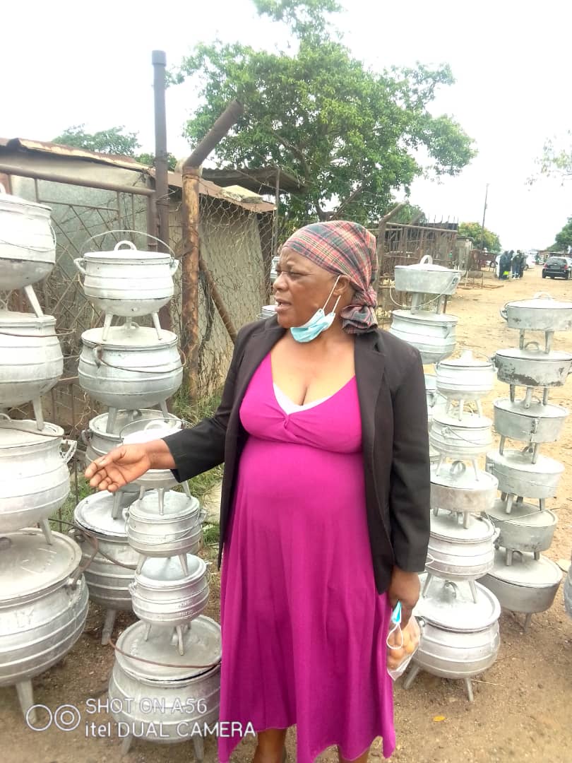 Chiwera in front of her aluminum pots made from plastic waste.