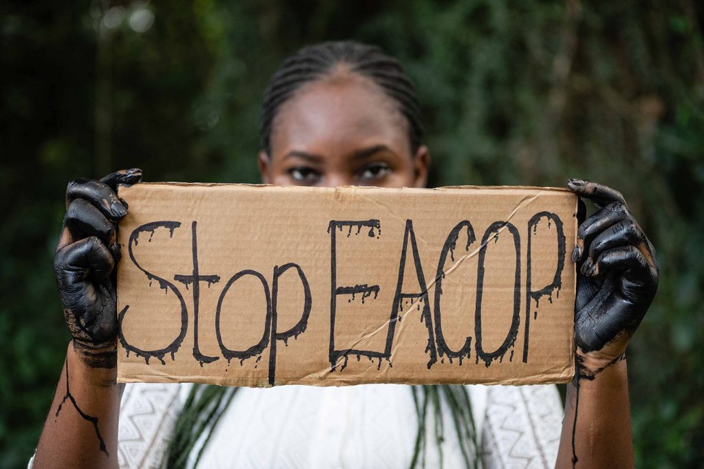 Person holding cardboard sign saying Stop EACOP