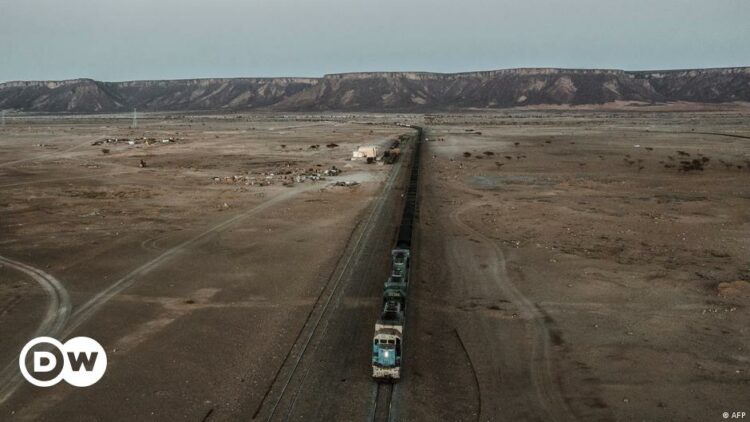 Aerial view shows a freight train on a track running down the centre of the image, with a tableland ridge visible in the background