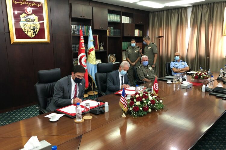 Four men sit at a table; two men sign a document.