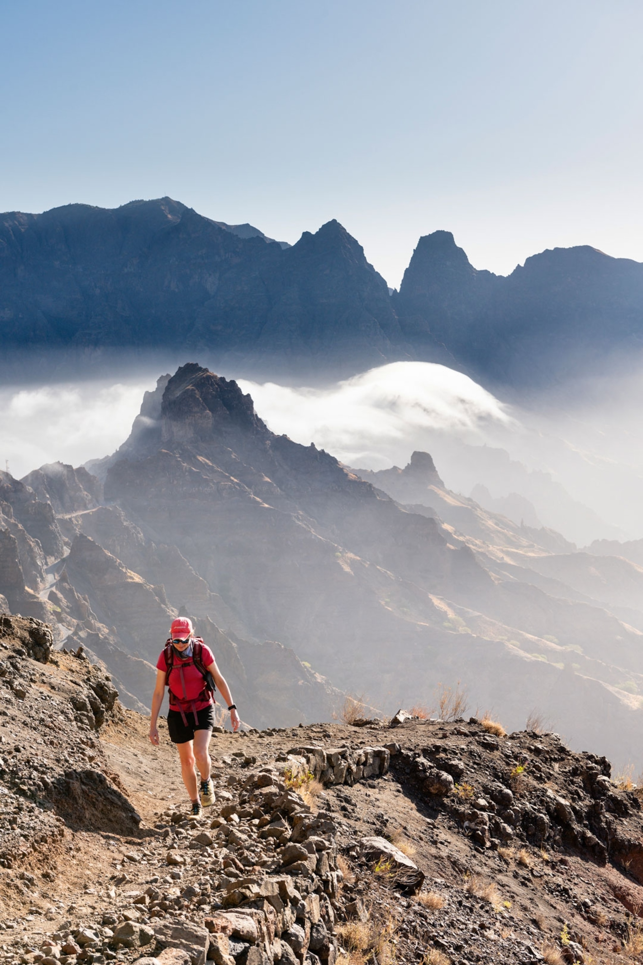 Hiker walking on rocky terrain surrounded by mountain peaks and hazy mist