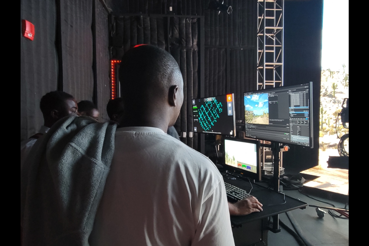 Man seen from behind as he observes several screens displaying images of data and landscapes.