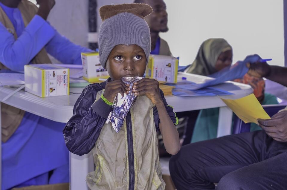 A young boy at a displacement camp nutrition support center in Maiduguri, Nigeria, eats from a packet of Ready-to-Use Therapeutic Food provided by UNICEF to treat acute malnutrition.