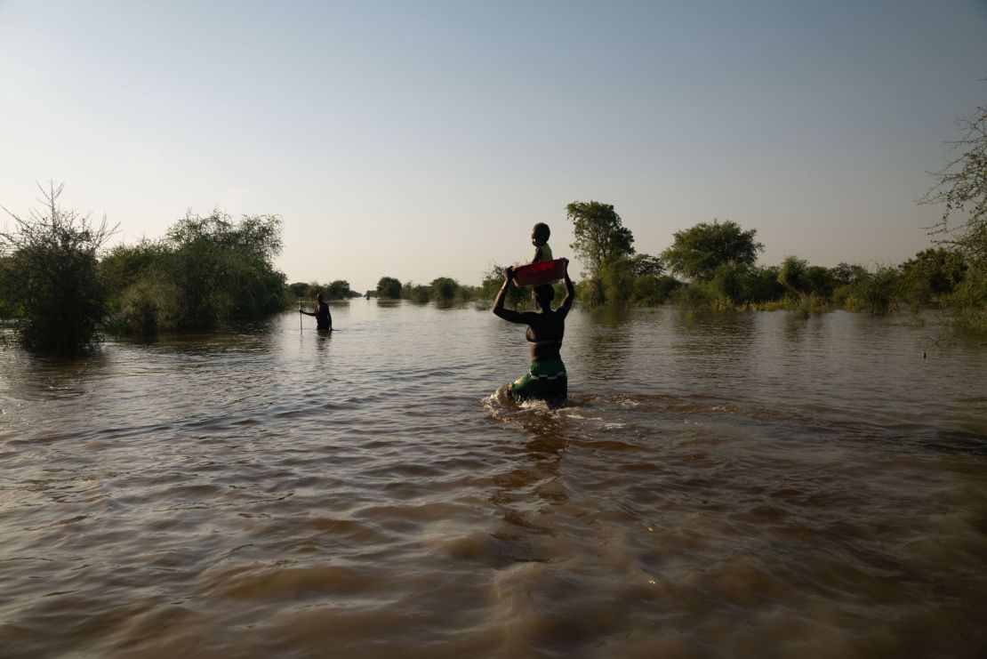 A woman carries her baby on her head as she wades through the floodwaters.