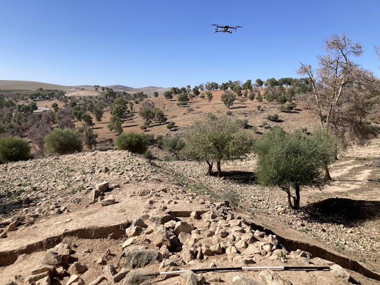 A drone flies above a rocky outcrop that reveals stones and ridges and suggests an archaeological dig.