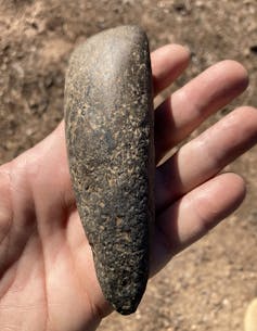 A hand holds a smooth black rock that has been shaped into a point on one end.